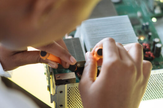 Crop of ethnic system administrator in uniform using screwdrivers and checking motherboard on electronic equipment during work in repair department